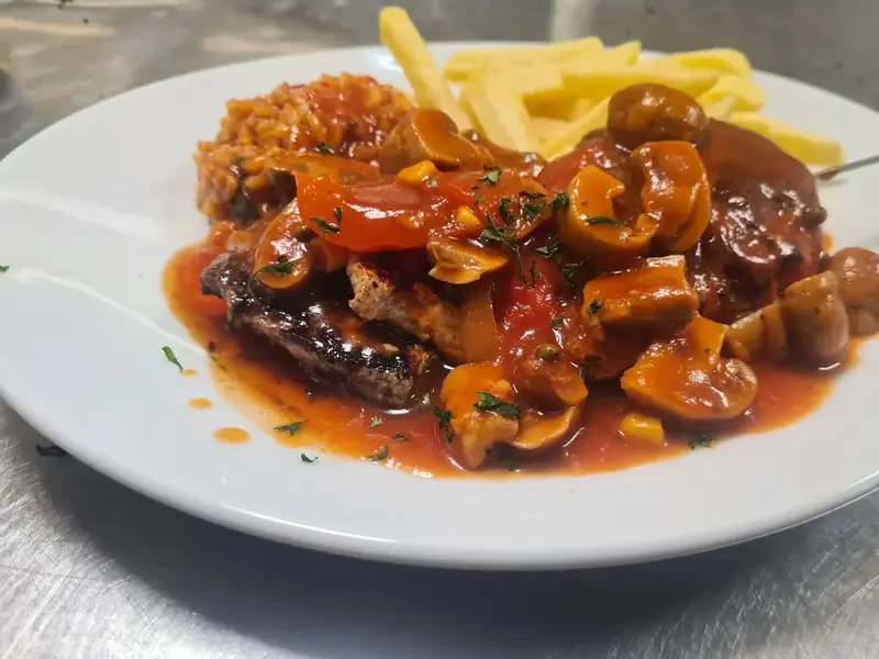 Fleischgericht mit Soße aus Champignons, Tomaten und Paprika, dazu Djuvec-Reis und Pommes frites